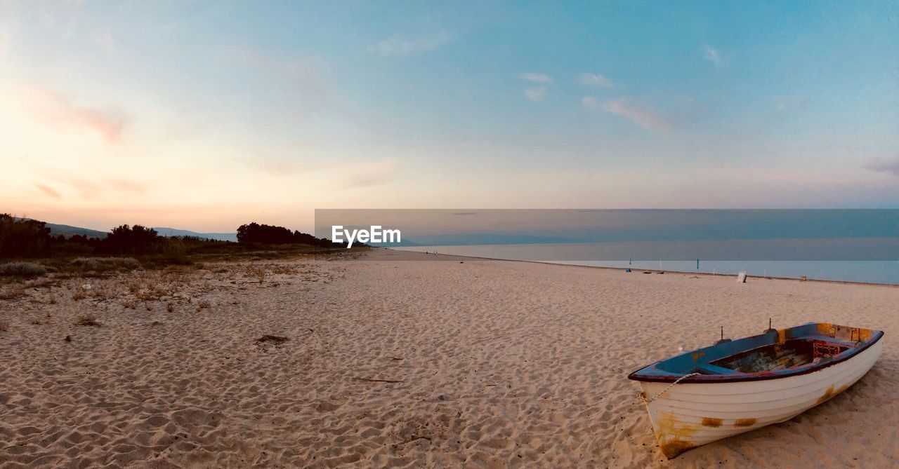 BOATS MOORED ON BEACH AGAINST SKY DURING SUNSET