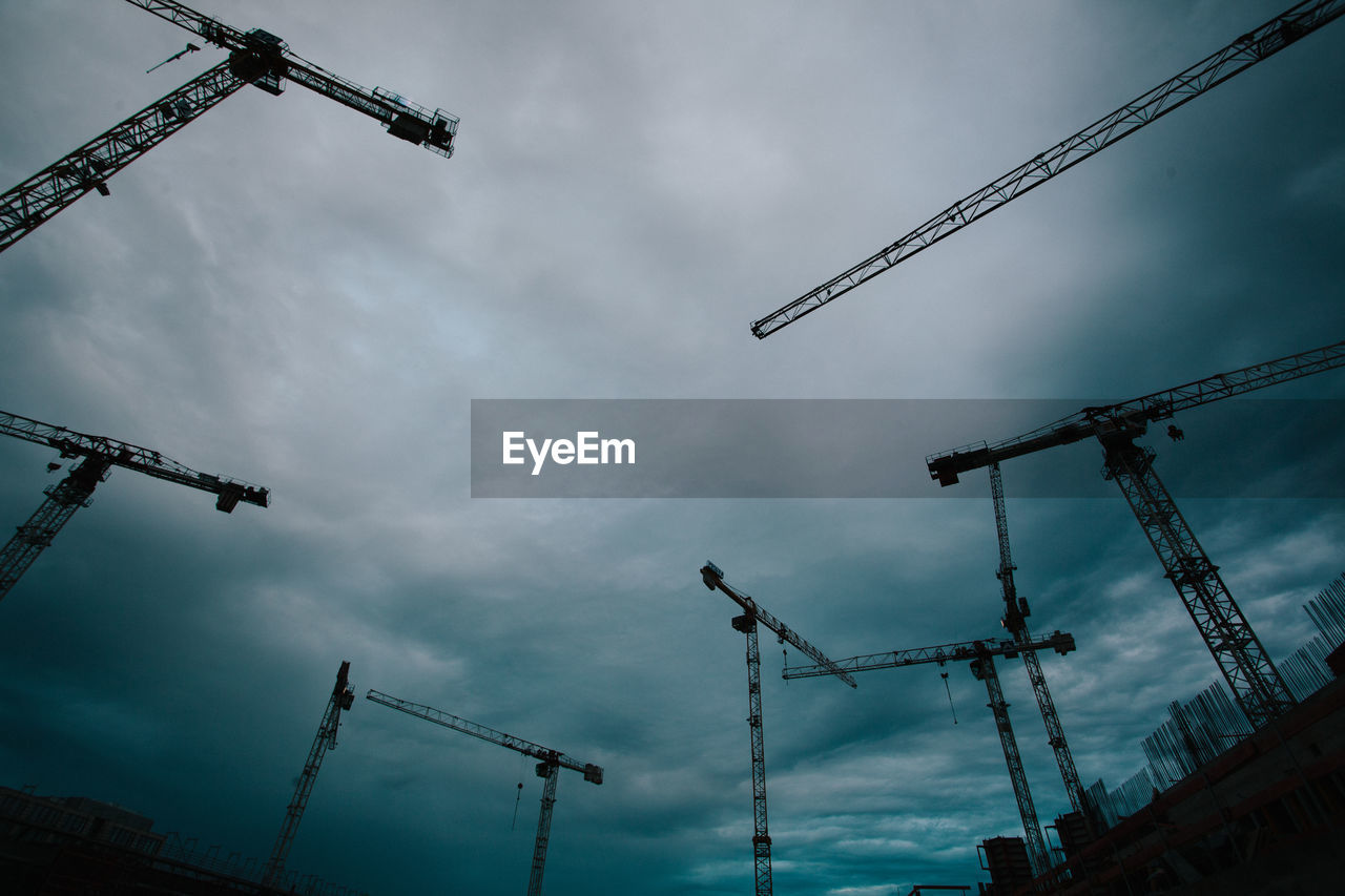 Low angle view of cranes against cloudy sky