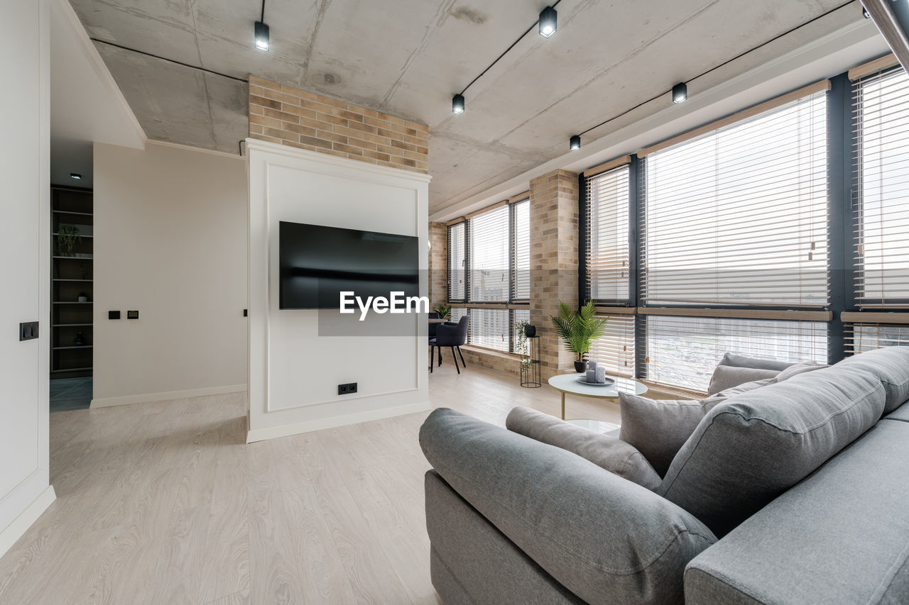 Interior in a modern style and a view of the tv and part of the kitchen near the large windows 