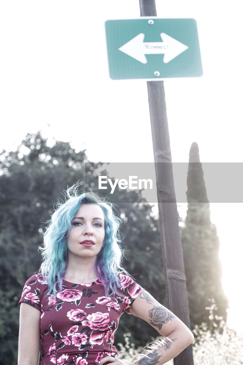 Portrait of beautiful female hipster standing against directional sign