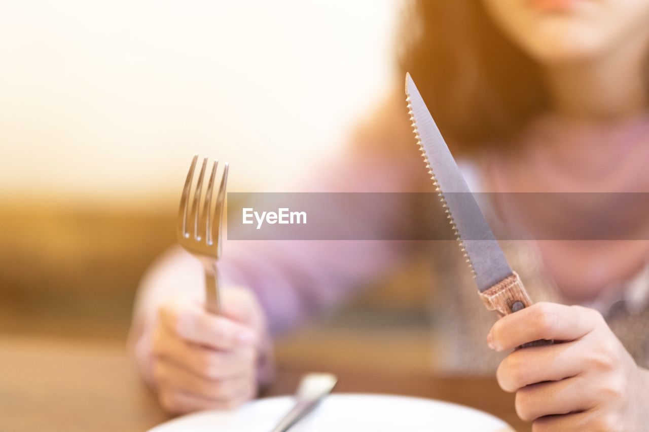 Midsection of woman with table knife and fork