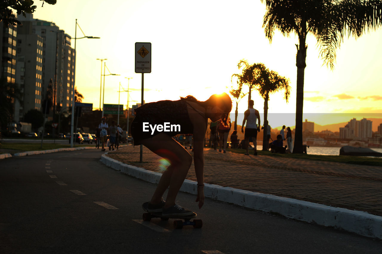 Full length of young woman skateboarding on road during sunset