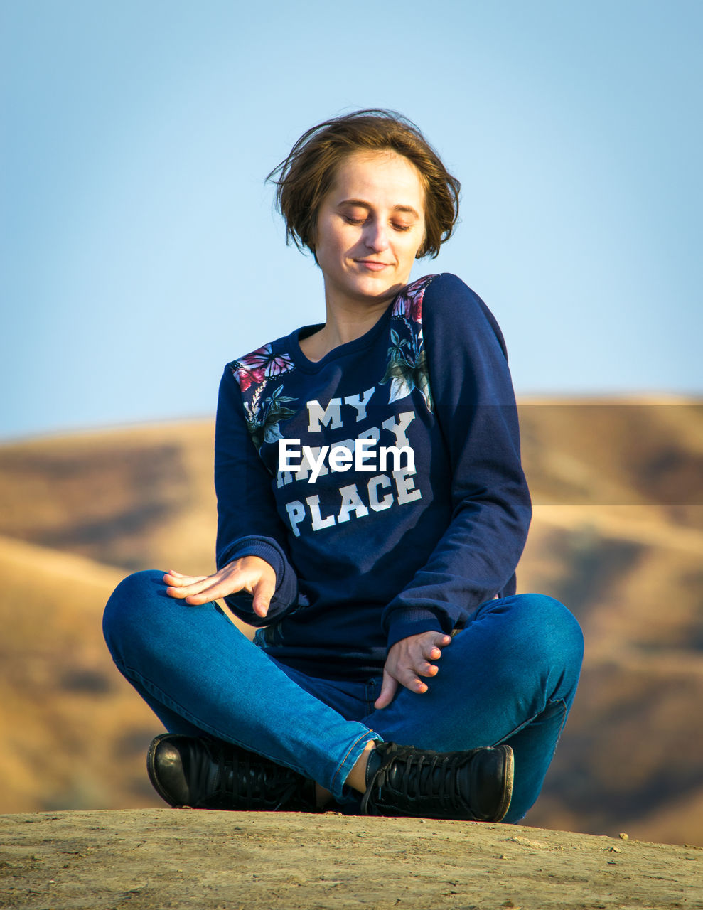 PORTRAIT OF HAPPY YOUNG WOMAN SITTING AGAINST CLEAR SKY