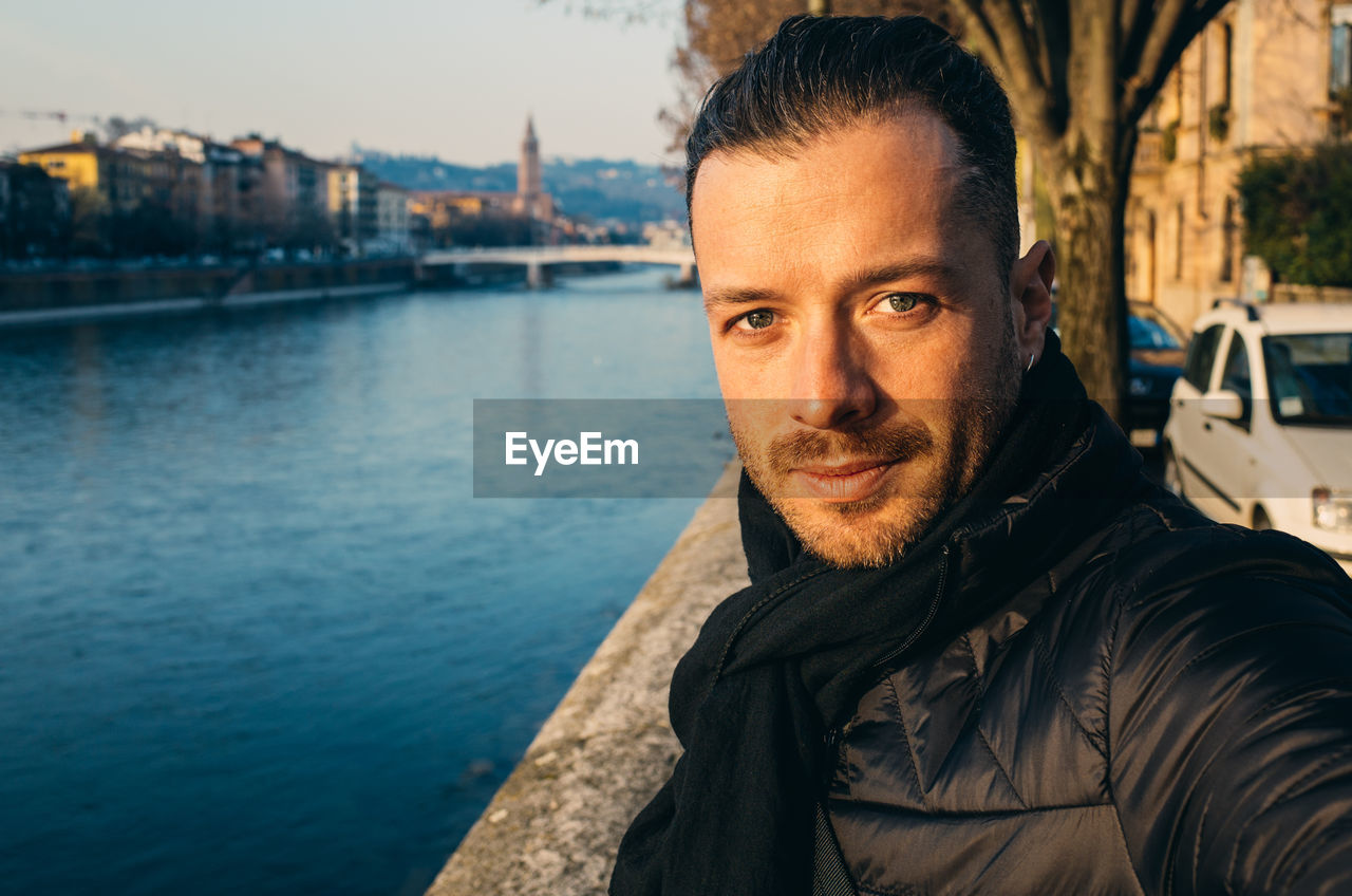 Portrait of handsome man standing by river against sky