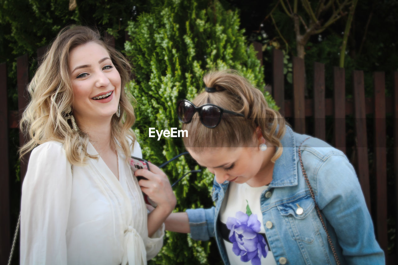 Portrait of smiling young woman with sister standing outdoors