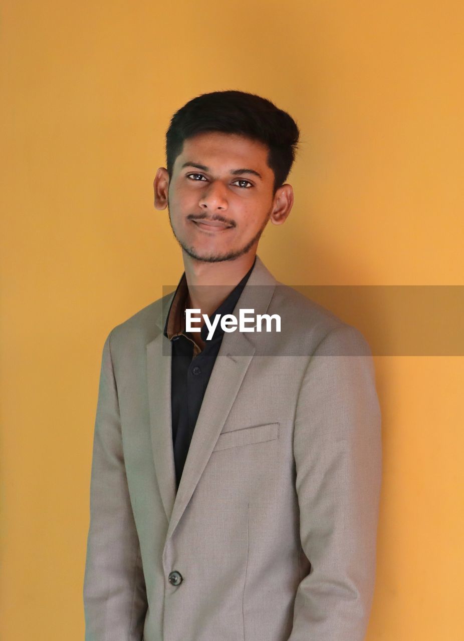 Portrait of young man standing against yellow background