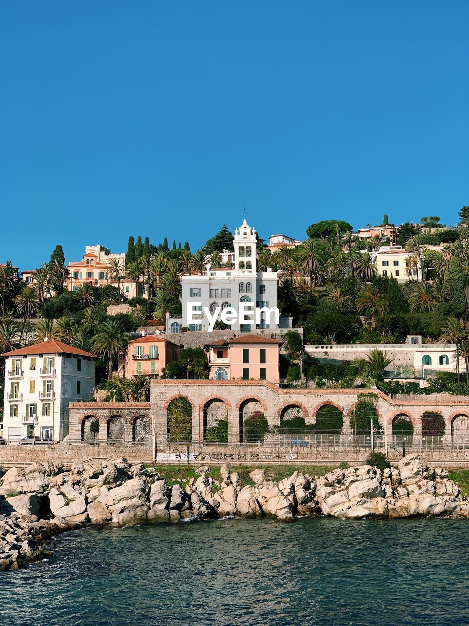 Buildings by sea against clear blue sky