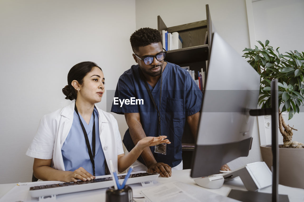 Doctor explaining young male colleague over desktop pc in clinic