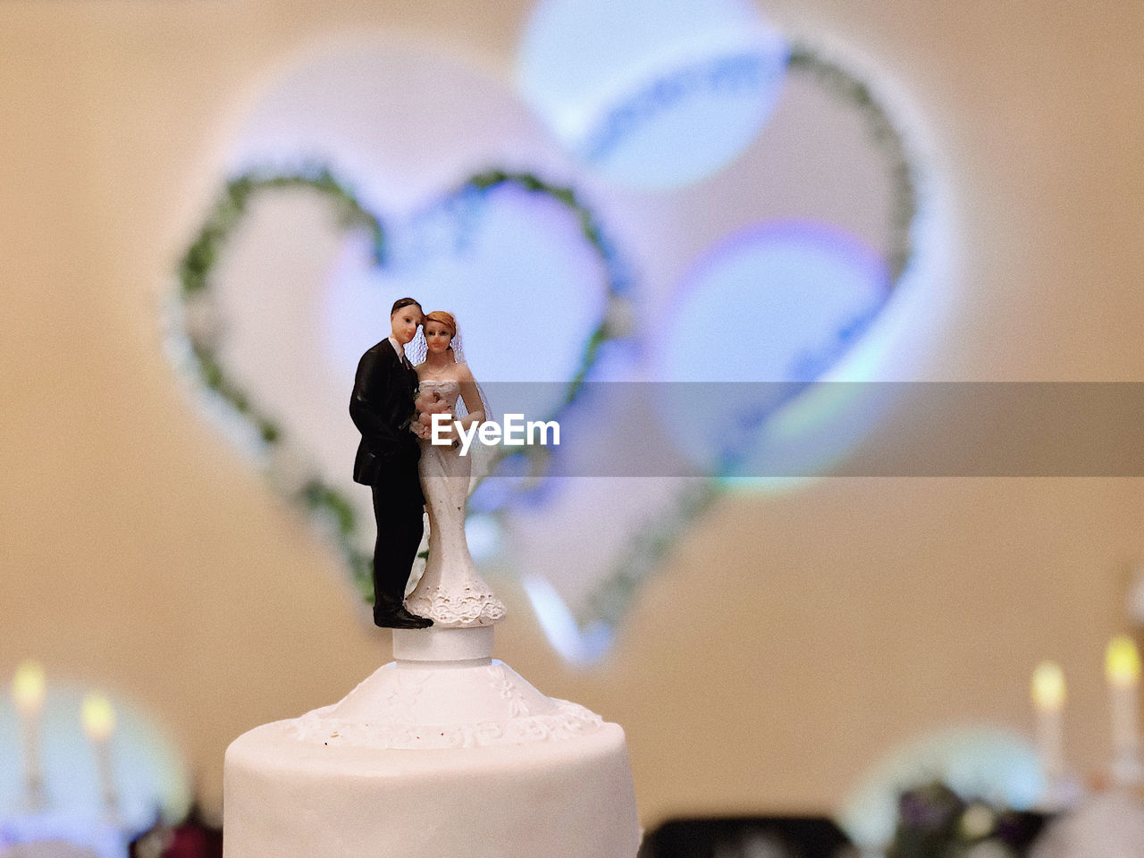 Close-up of a wedding cake focused on sugar couple on top with heart shapes and bokeh