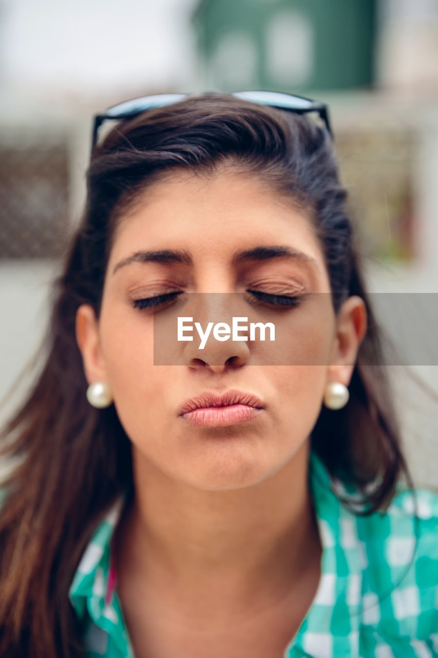 Close-up of young woman with eyes closed puckering lips while standing outdoors