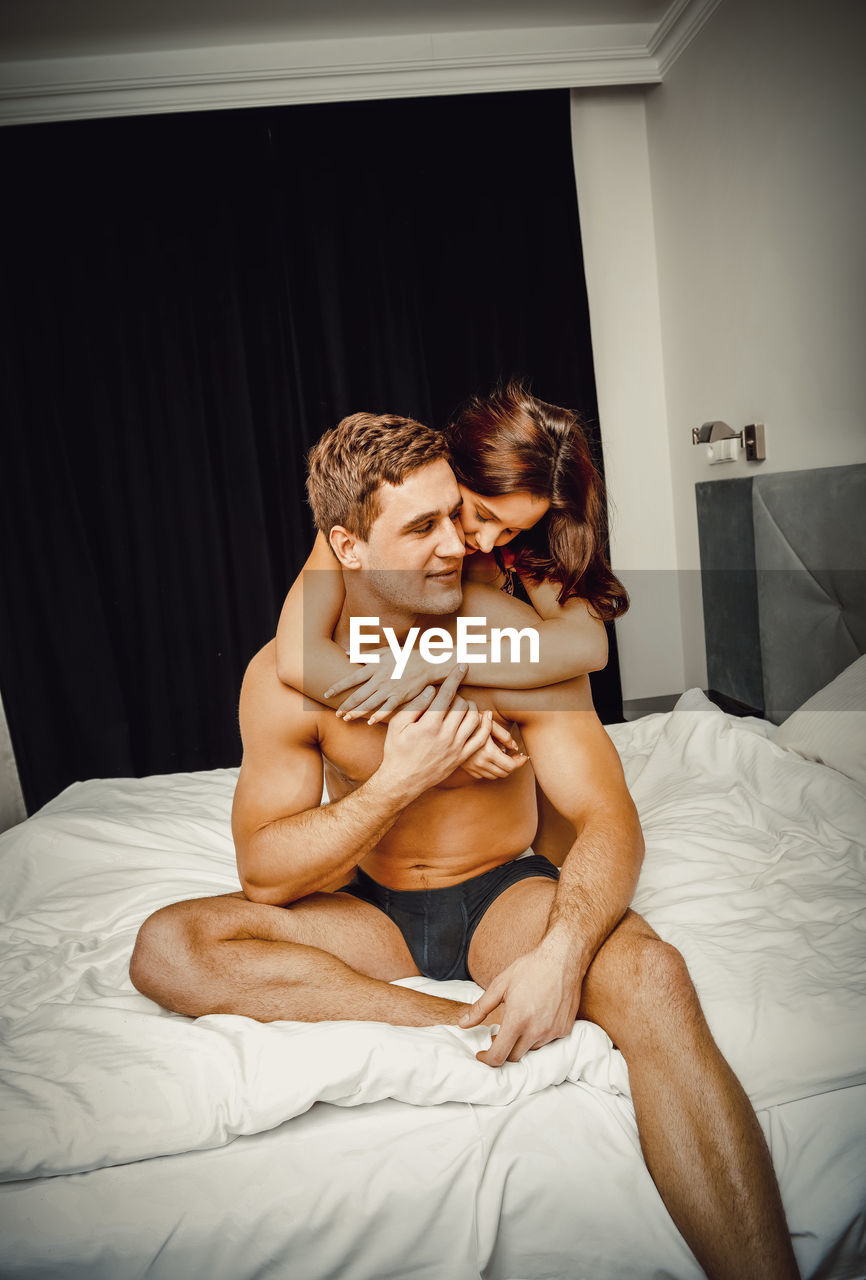 Shirtless couple romancing on bed at home