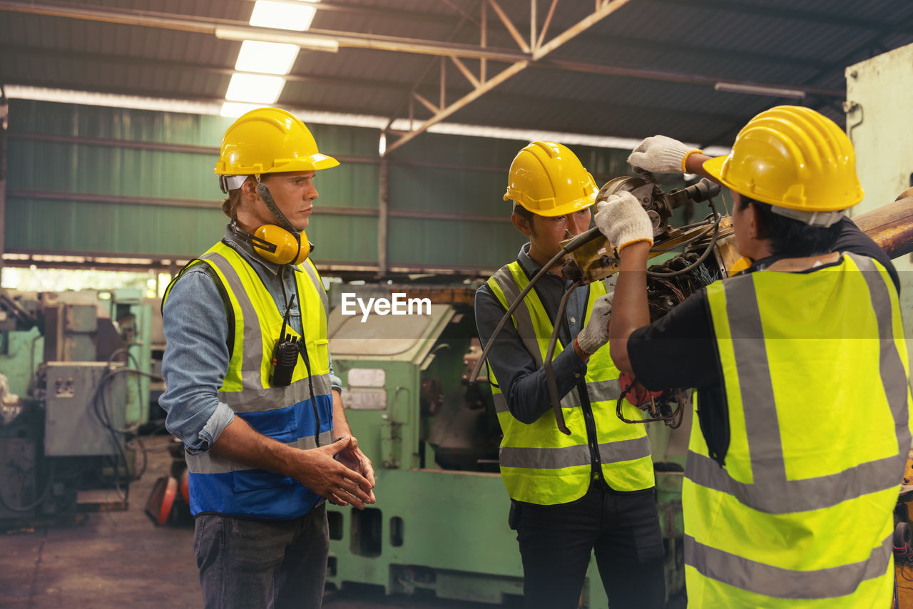Engineers in an industry plant setting up machines vs a background of a machine factory.