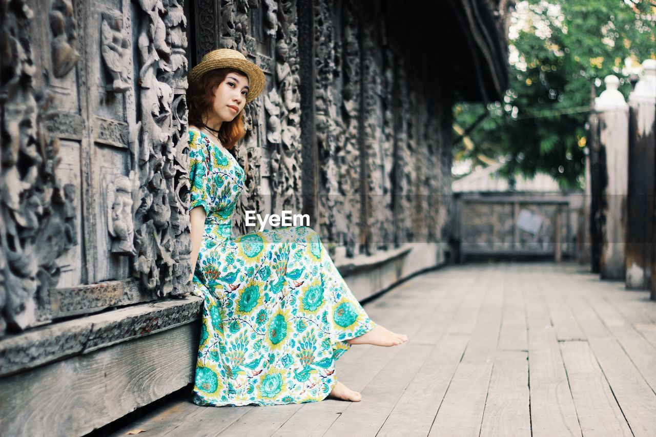 Young woman looking away while sitting on retaining wall at temple