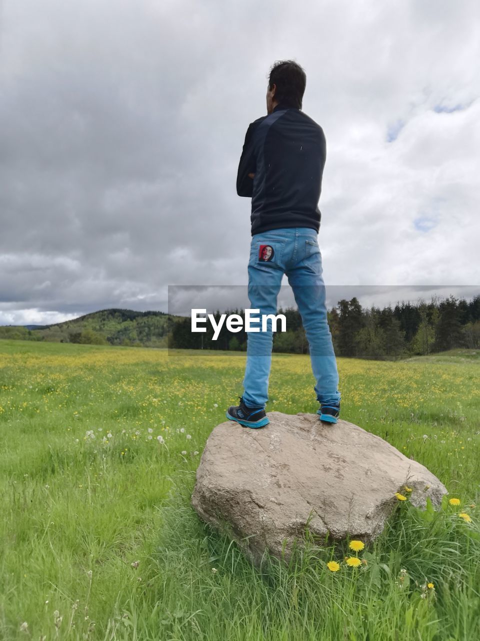 FULL LENGTH REAR VIEW OF MAN STANDING ON FIELD AGAINST SKY