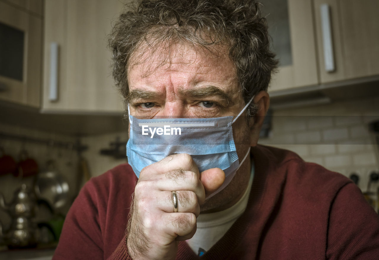 An adult man in a medical mask on his face is coughing at home. coronavirus pandemic concept