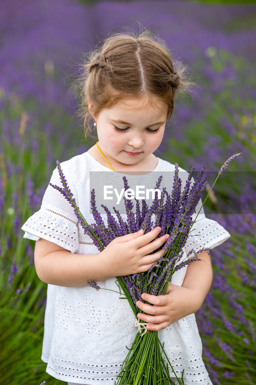 LOW ANGLE VIEW OF GIRL STANDING ON FIELD AGAINST PURPLE FLOWERING PLANTS