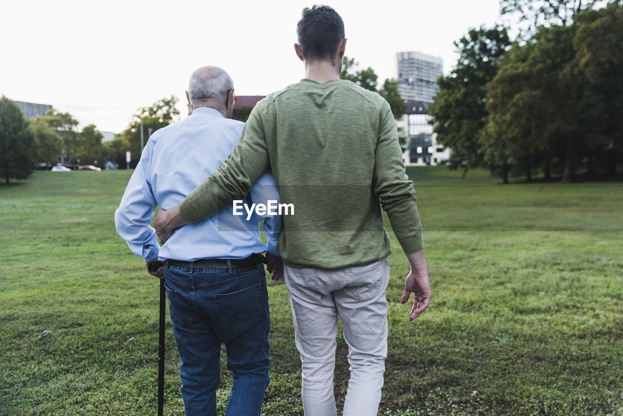 Back view of young man assisting his grandfather walking