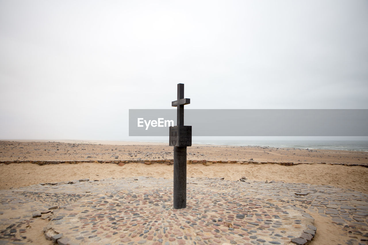 Religious cross at beach against sky