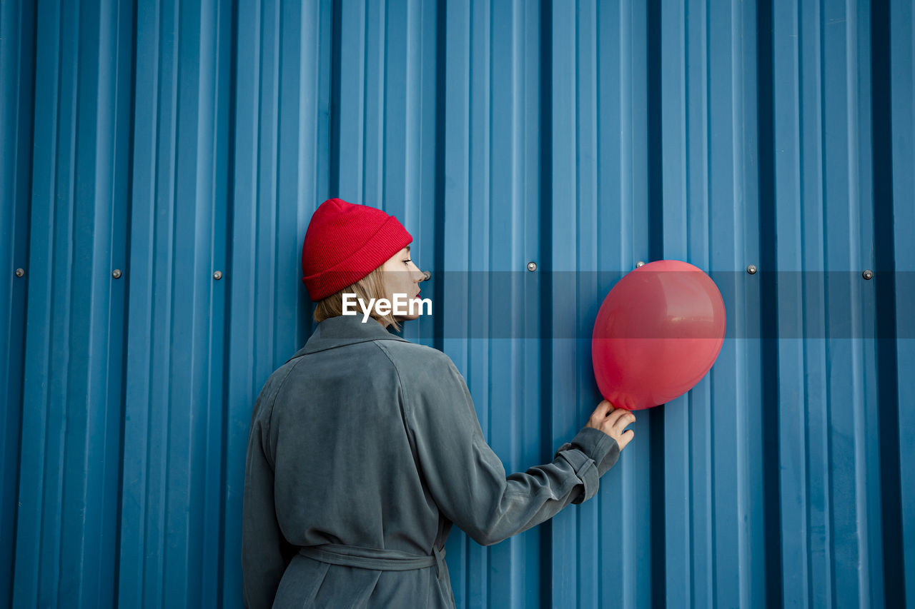 Mid adult woman holding red balloon by blue shutter