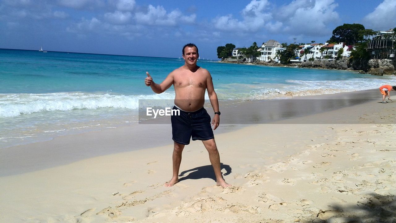 Shirtless man gesturing thumbs up sign at beach