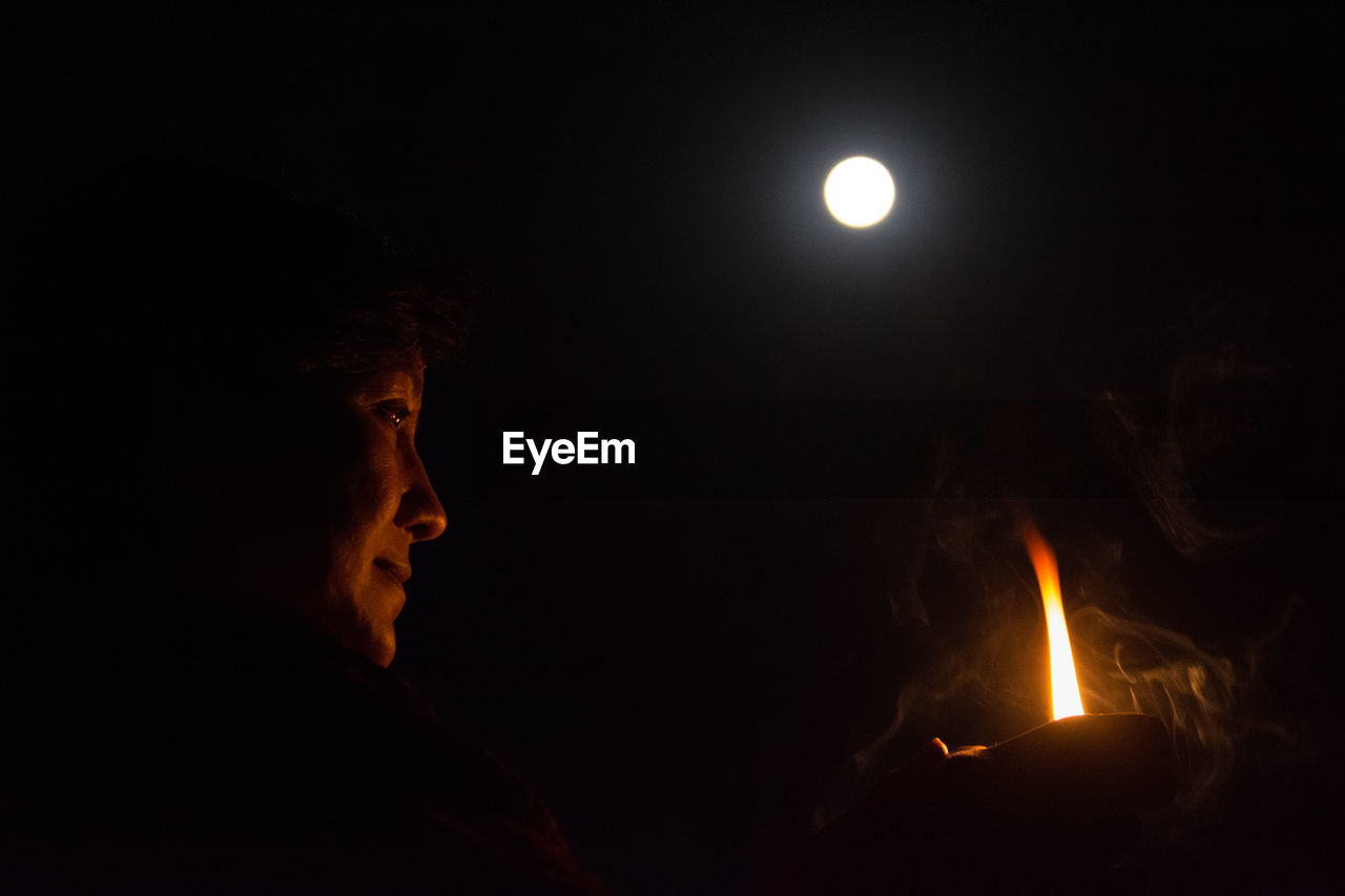 Low angle view of person holding diya against moon at night