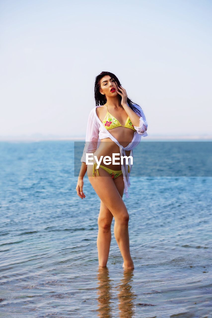 Seductive woman wearing bikini while standing in sea against sky