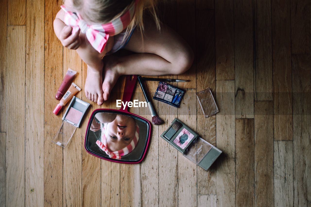 Directly above shot of girl playing with beauty products on hardwood floor