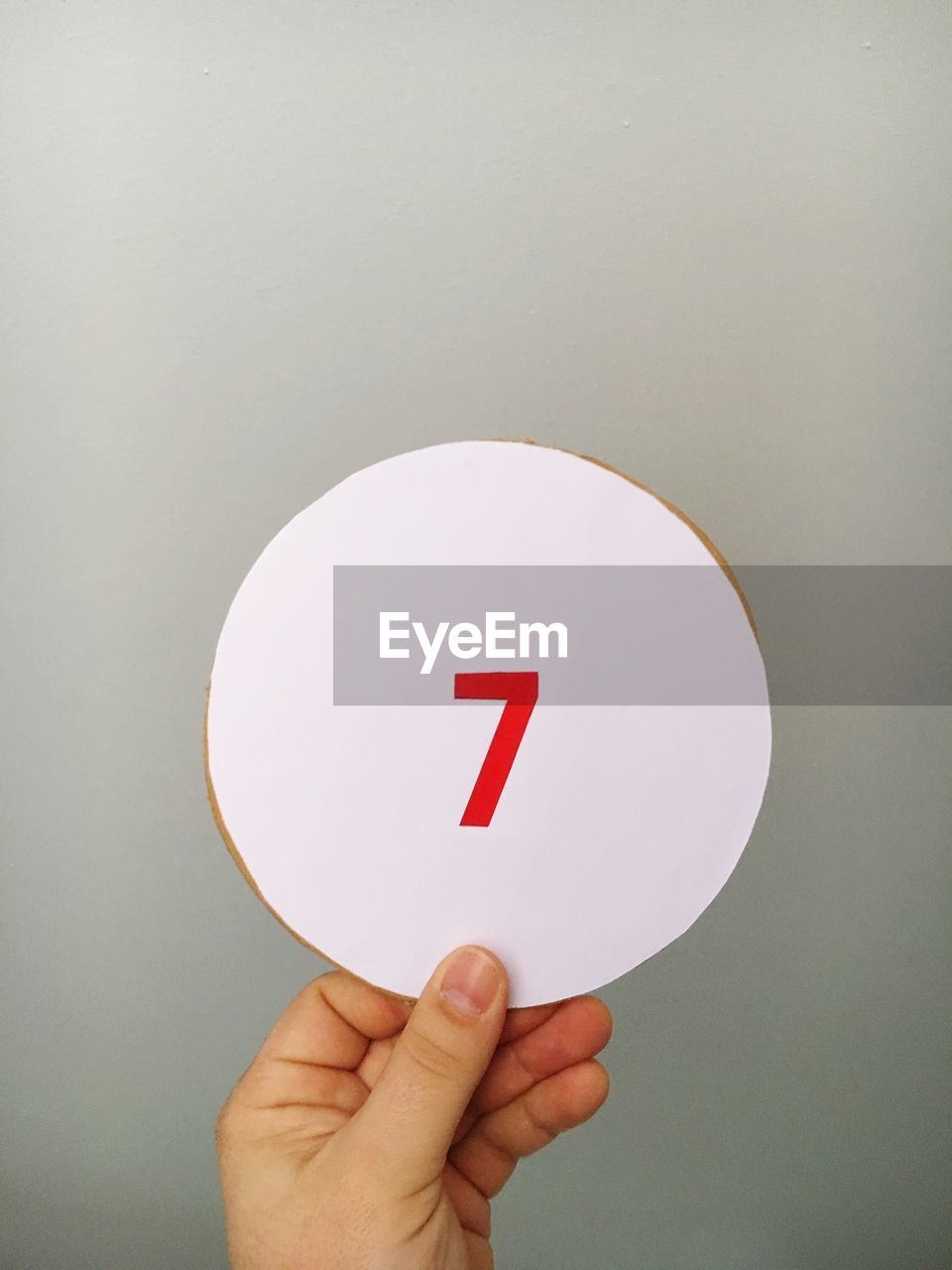 Cropped hand of person holding number on cardboard against gray background