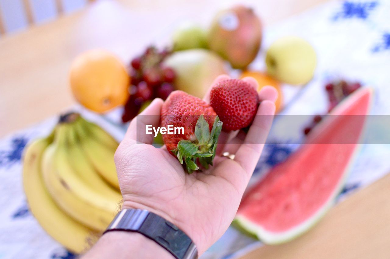 Close-up of cropped hand holding strawberries at home