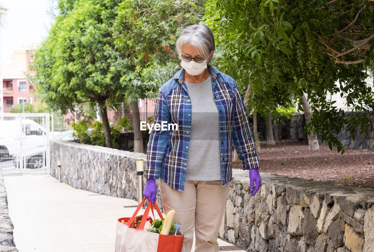 Senior woman holding groceries bag standing by plants
