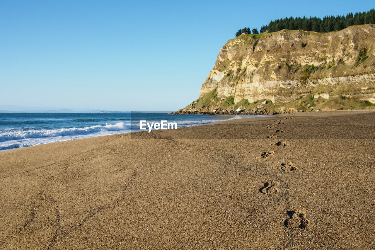 Footprints on beach by mountains against clear blue sky