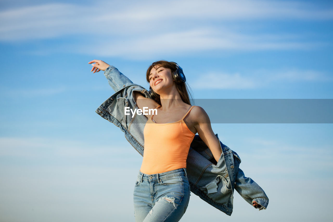 Cheerful young woman standing against sky