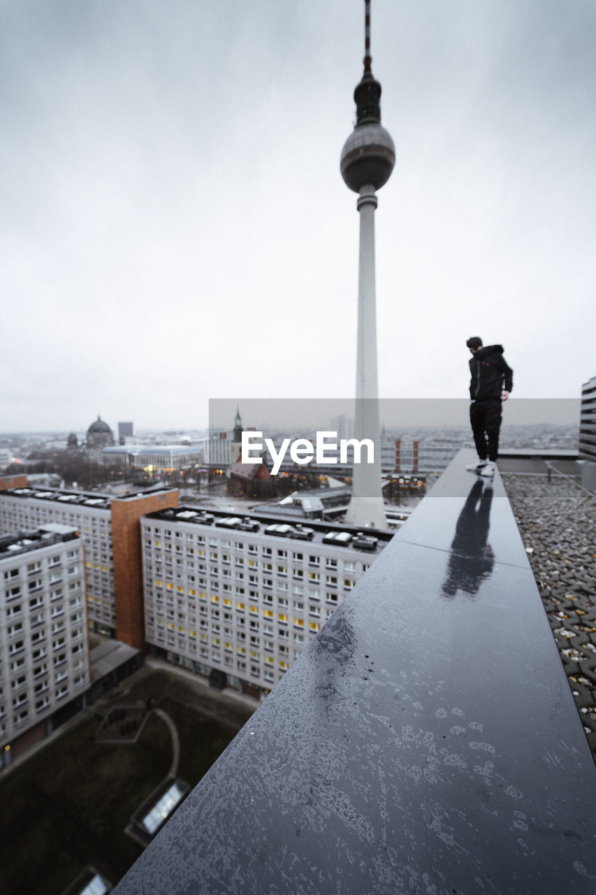 Rear view of young man walking on building against clear sky in city