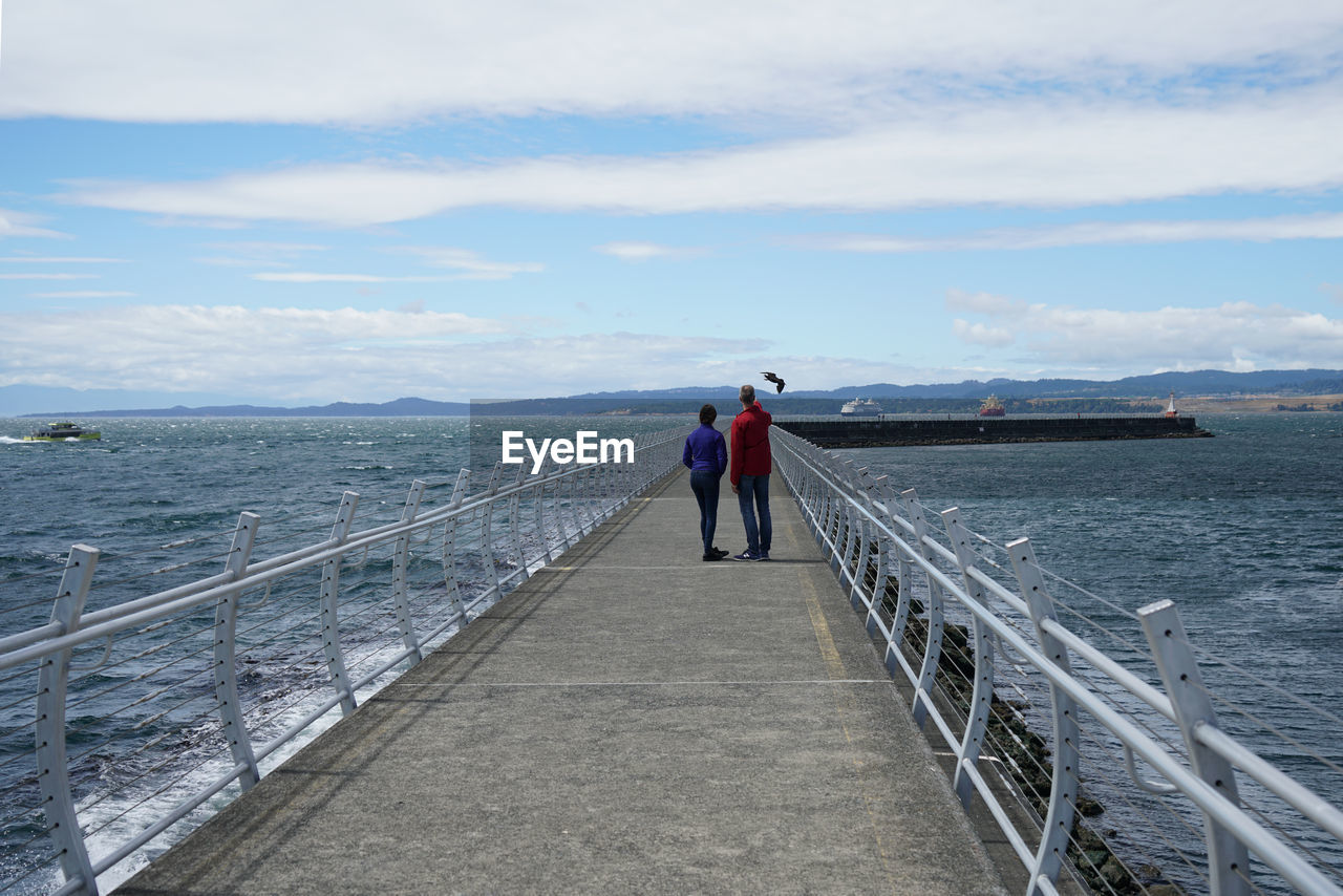 Rear view of friends standing amidst sea on pier