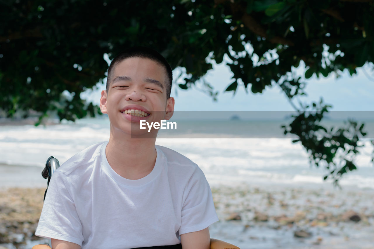 Close-up of smiling boy sitting on wheelchair against sea