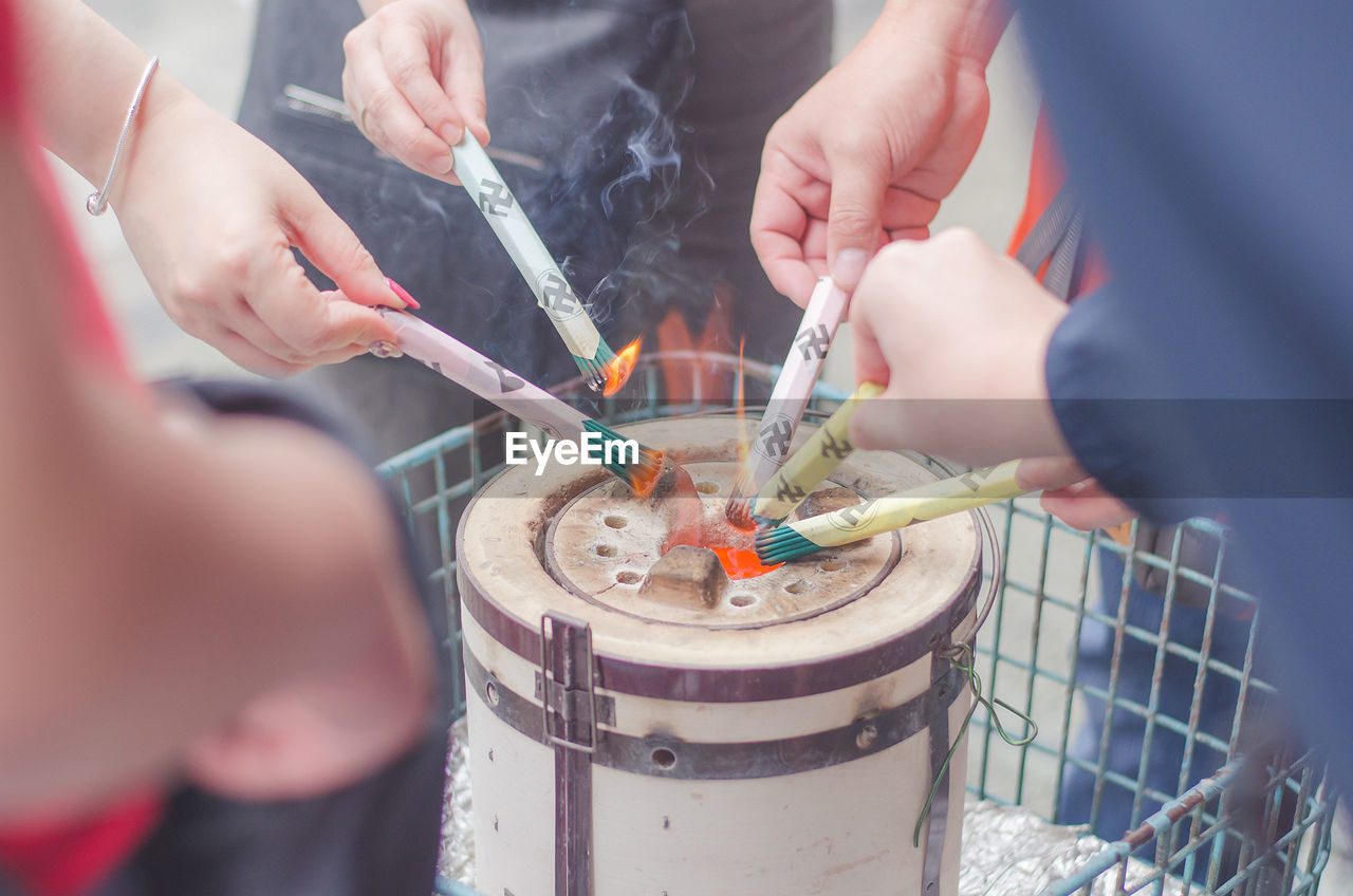 Cropped hands of people burning incense sticks at temple