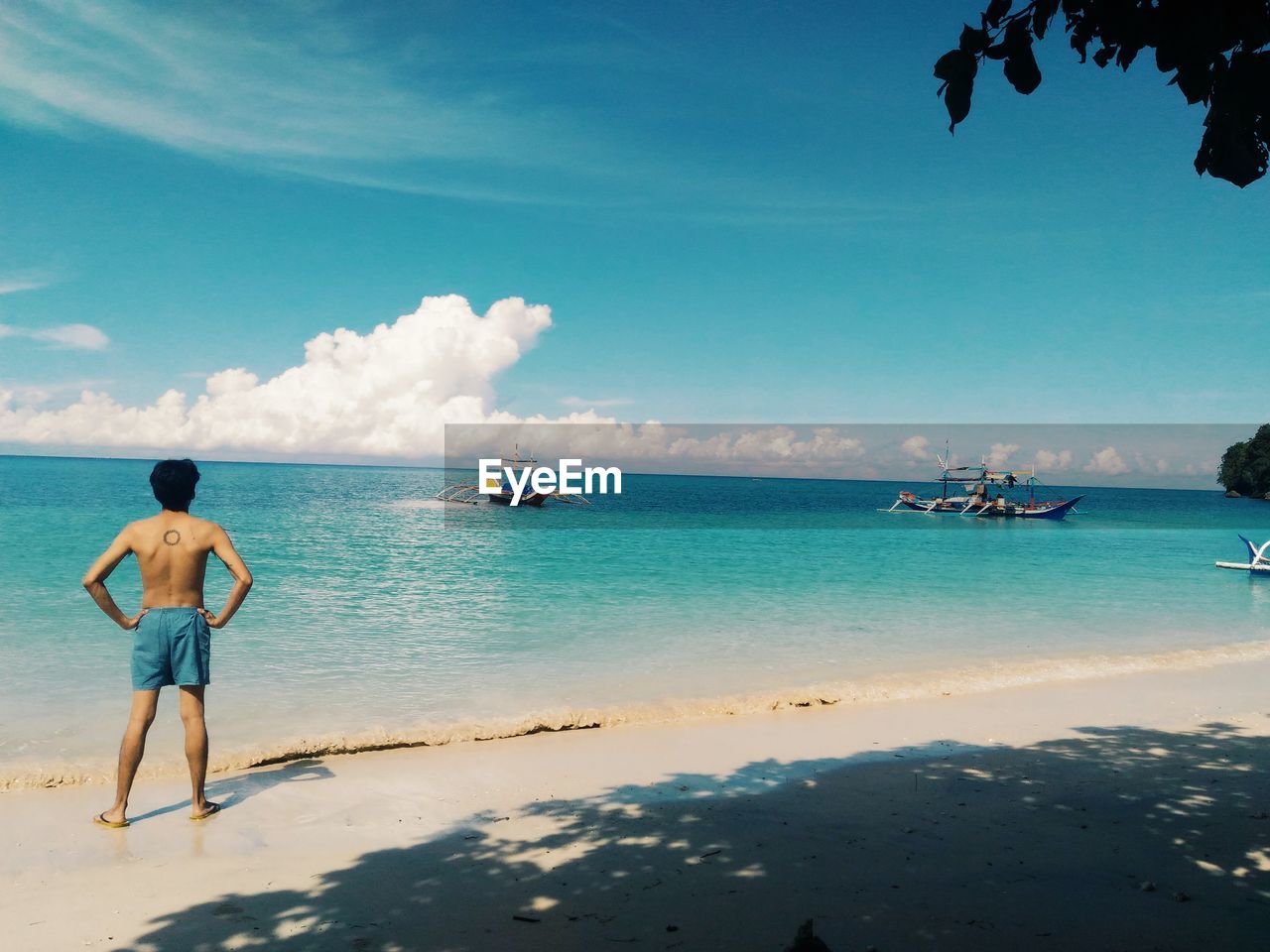 Rear view of man standing at beach against blue sky