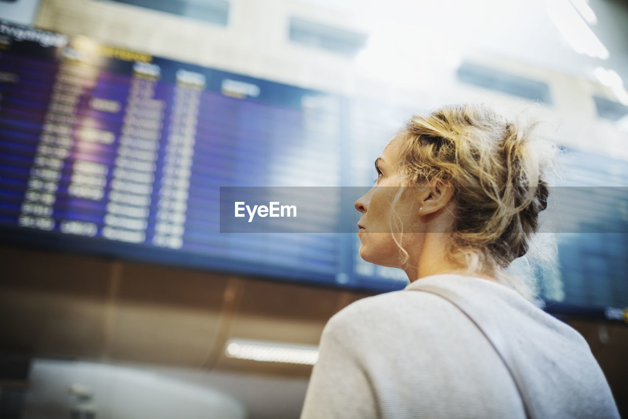 Rear view of businesswoman looking at arrival departure board in airport