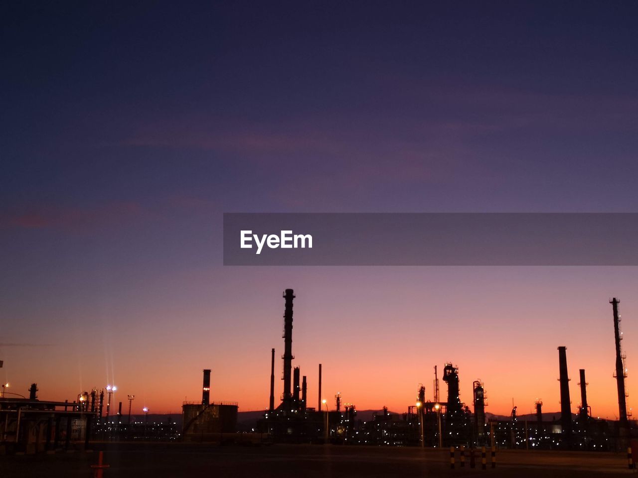 Silhouette factory against sky during sunset