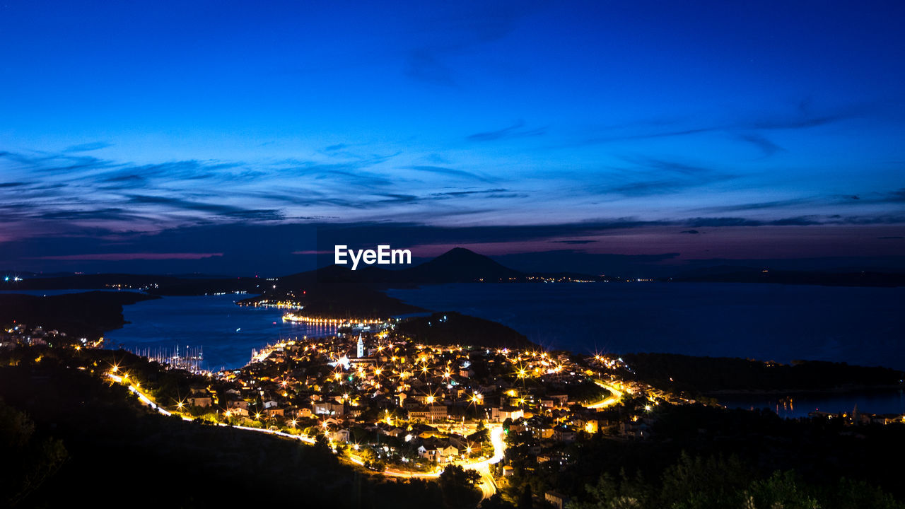 High angle view of illuminated city by sea against sky at night