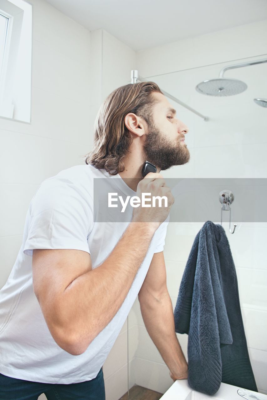 Young man shaving beard at domestic bathroom