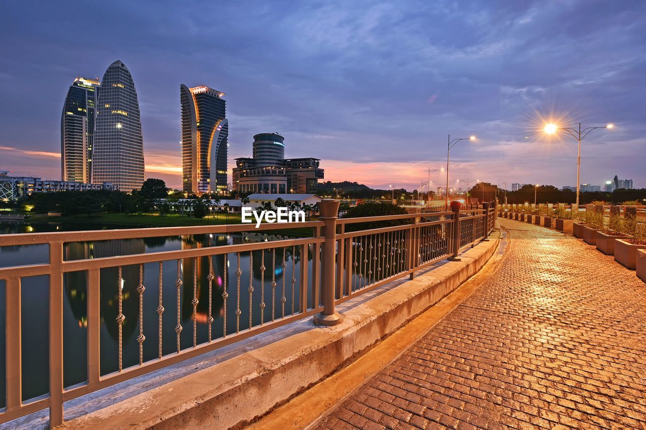 Illuminated footpath in city against sky at dusk