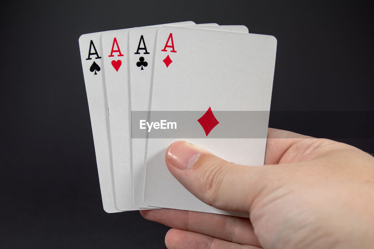 Cropped image of hand holding ace playing card against black background