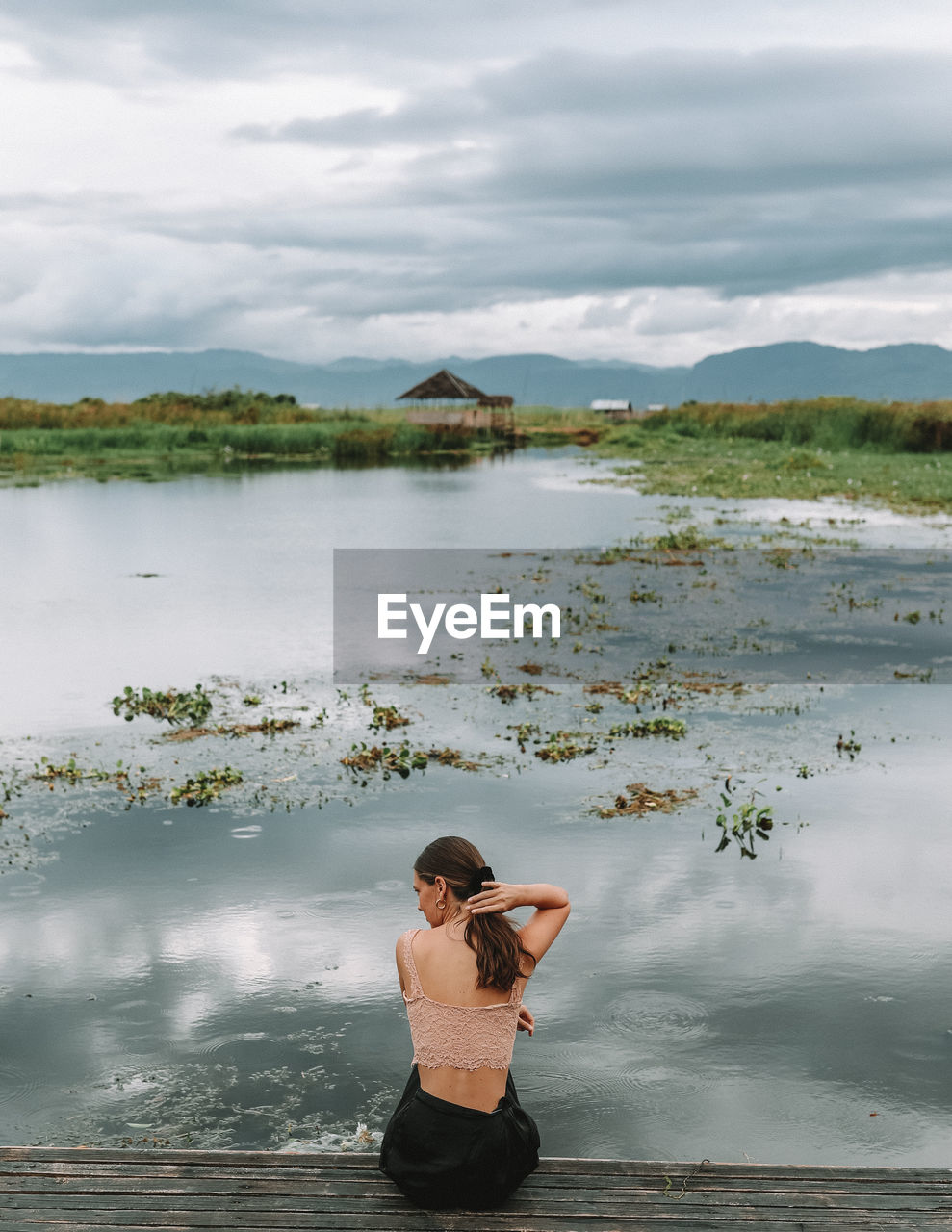 Rear view of woman sitting on pier over lake against sky