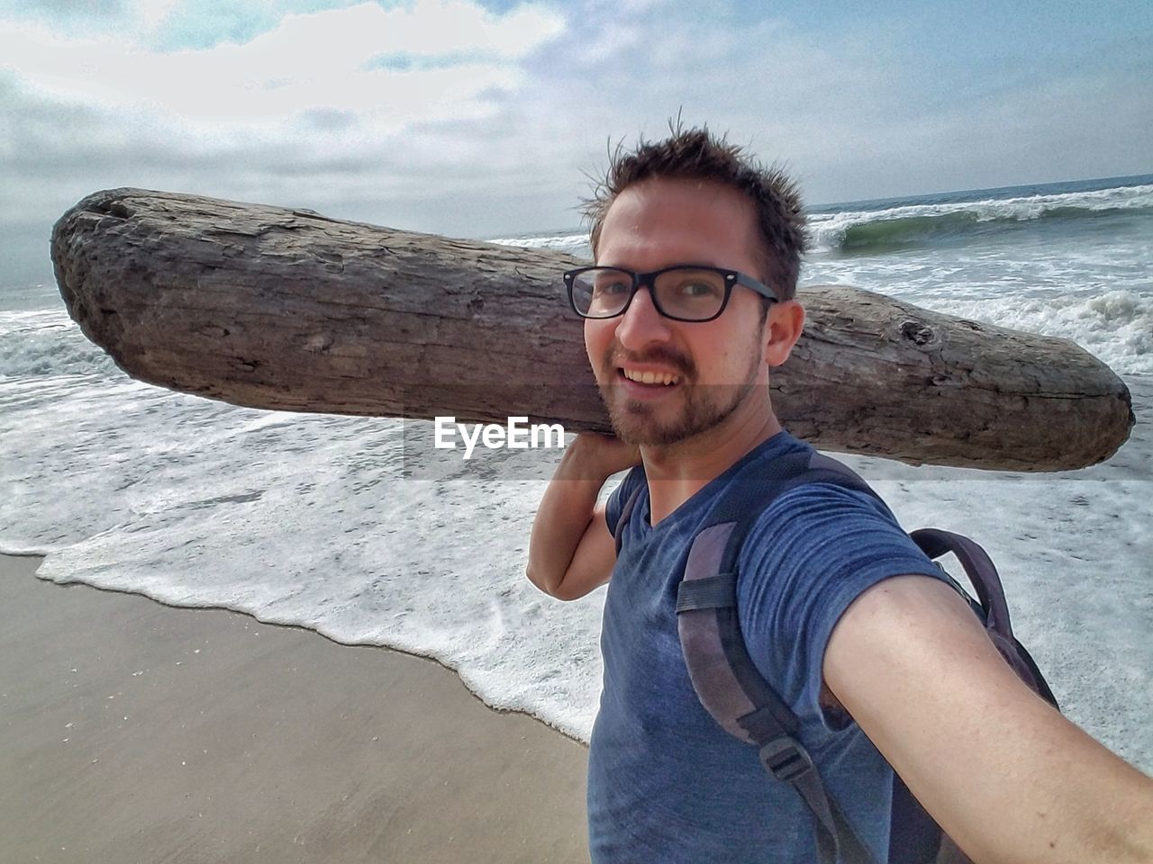 PORTRAIT OF YOUNG MAN WEARING SUNGLASSES ON BEACH