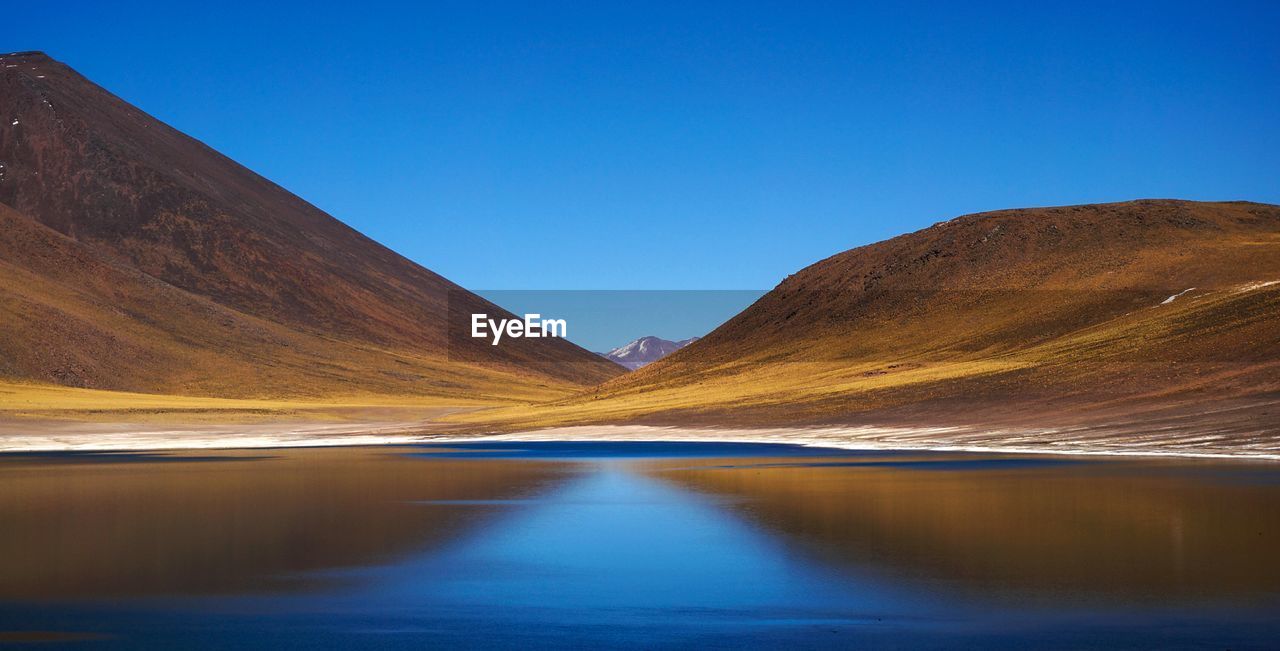 Scenic view of lake and mountains against clear blue sky