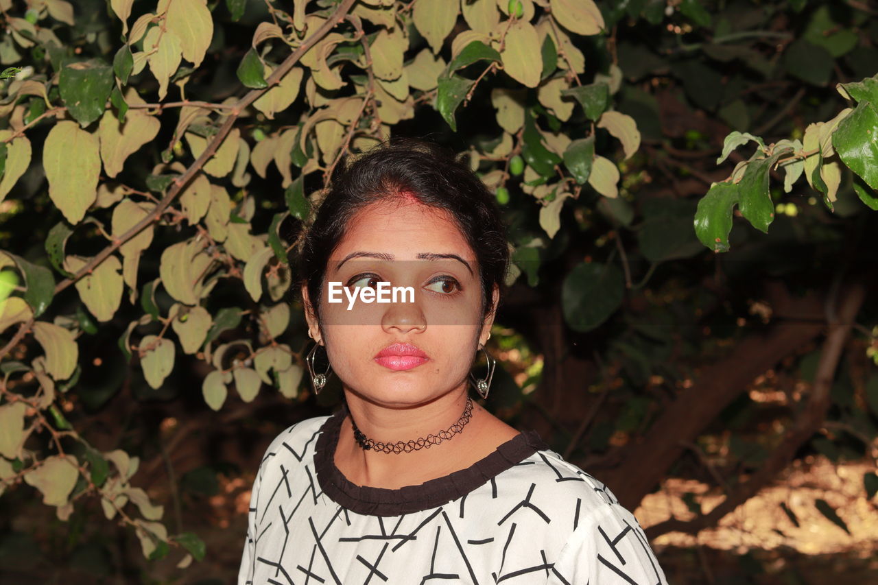 Beautiful young woman looking away against plants