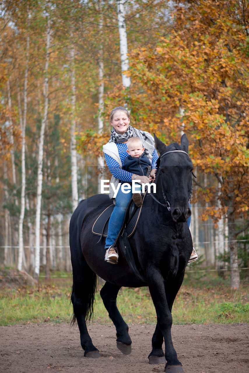 Woman sitting with baby boy on horse at field during autumn