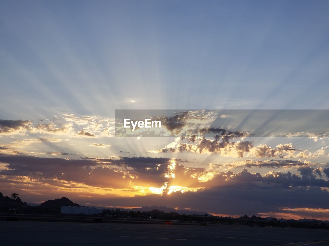 SUNLIGHT STREAMING THROUGH SILHOUETTE LANDSCAPE AGAINST DRAMATIC SKY