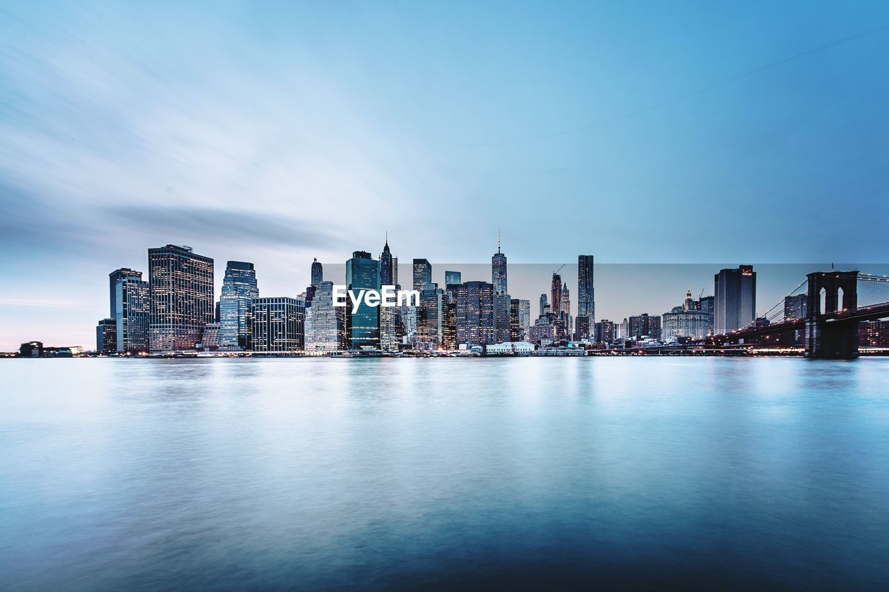 Sea by buildings in city against blue sky